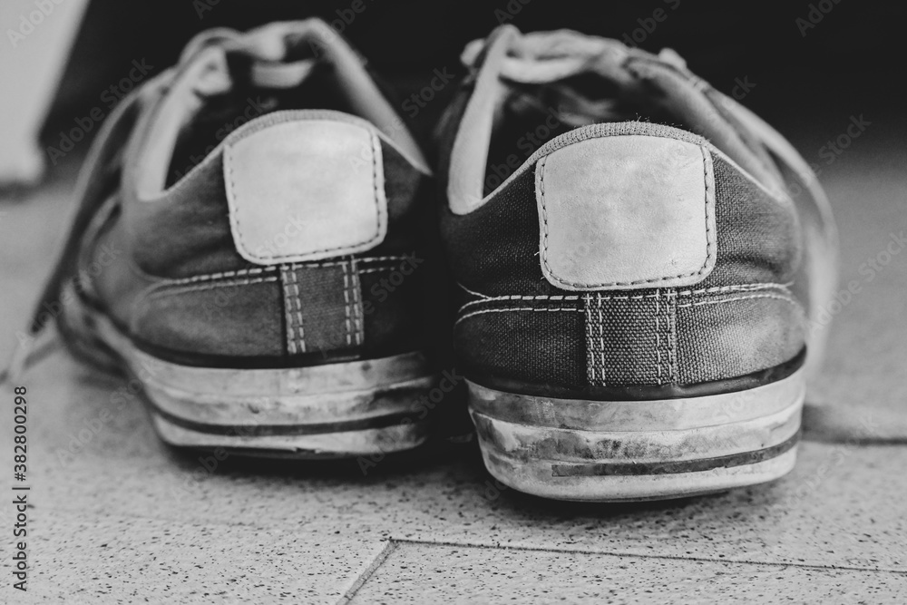 Black and white image shows hard used sneakers from the back side ...