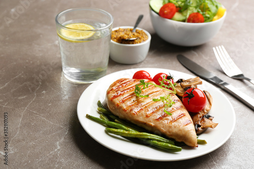 Tasty grilled chicken fillet with green beans and tomatoes on brown marble table