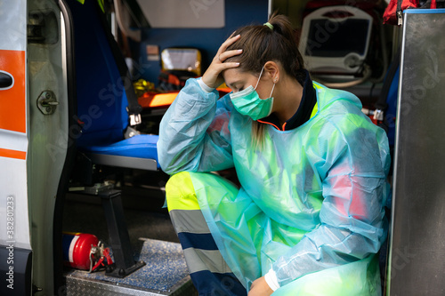 Portrait of a young woman doctor sitting on the ambulance resting exhausted where a first aid intervention during the Covid-19 pandemic, Coronavirus wearing a face mask - Rescue concept