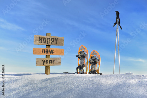 wooden sign with text happy new year in the snow next to snowshoes and ski sticks
