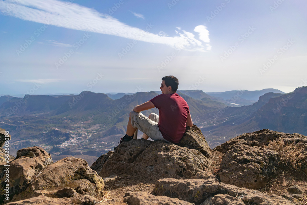 Young hiker resting and looking at the landscape from a peak Young hiker resting and looking at the landscape from a peak