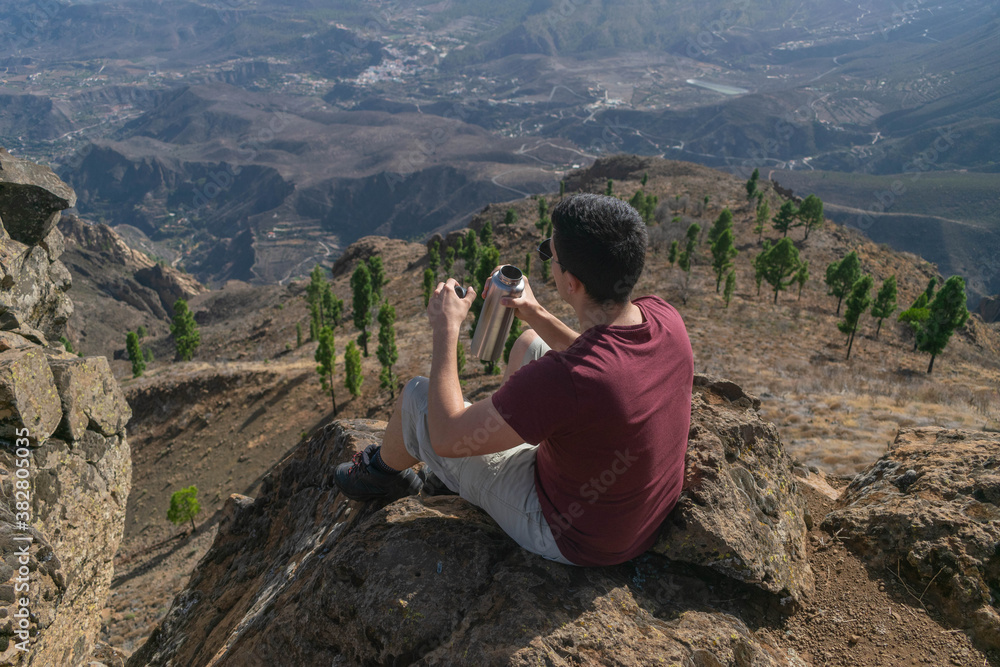 Naklejka premium Young hiker drinking water looking at the landscape from a cliff