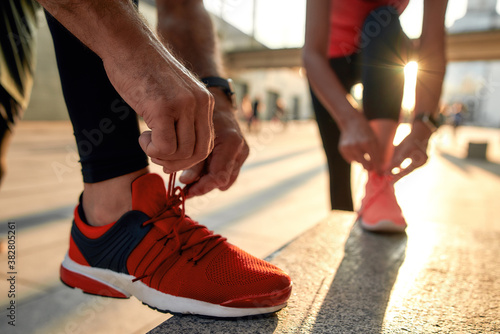 Close up photo of two people in sport clothes tying shoelaces before jogging
