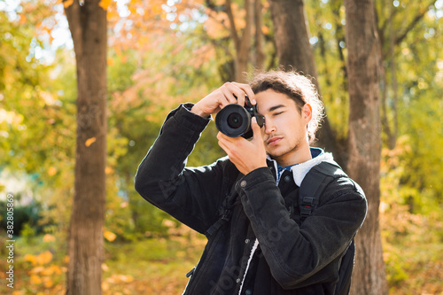 Amateur photographer with dark hair in black coat shooting in the park in autumn. Young man taking photos of fall landscapes in oktober.