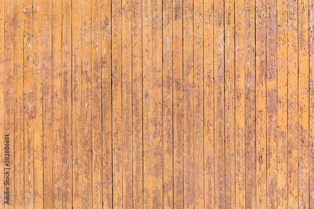 Narrow, vertically arranged boards with peeling yellow paint form a background, texture, pattern. Narrow, vertically arranged boards with peeling yellow paint form a background, texture, pattern.
