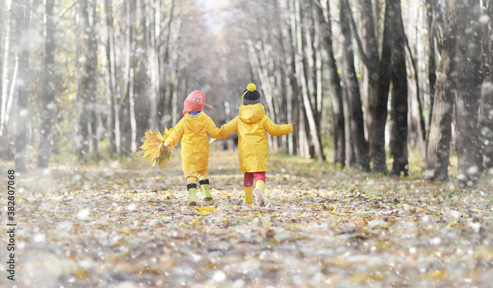 Fototapeta premium Toddlers on a walk in the autumn park. First frost and the first snow in the autumn forest. Children play in the park with snow and leaves.