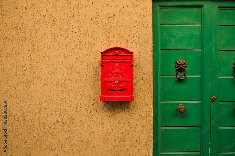 Red mailbox hanging on the wall of a house with a green door (