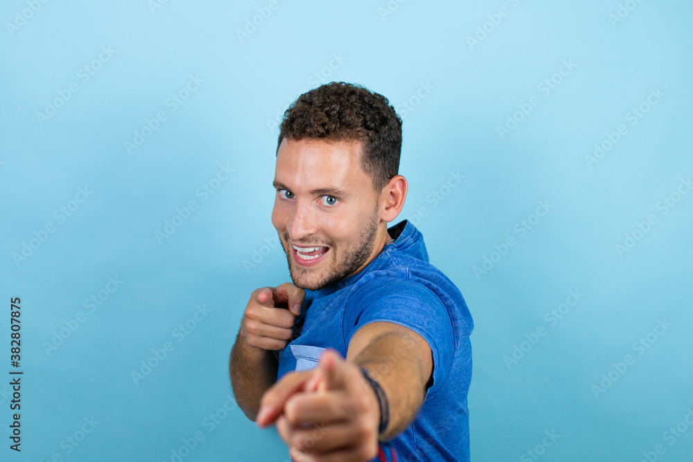Young handsome man wearing blue casual t-shirt over isolated blue background pointing to you and the camera with fingers, smiling positive and cheerful Young handsome man wearing blue casual t-shirt over isolated blue background pointing to you and the camera with fingers, smiling positive and cheerful