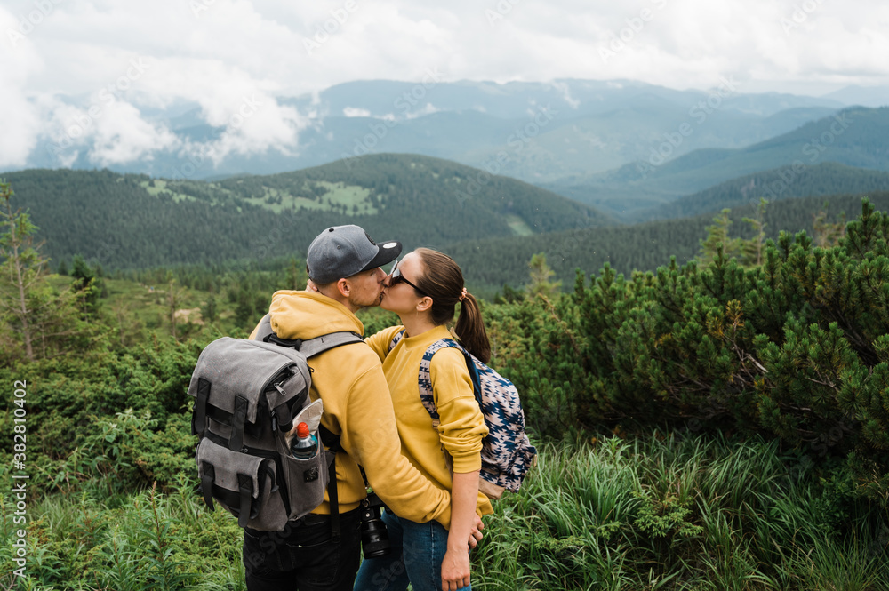 Couple of tourists, young man and woman in love kissing while climbing the mountain against the background of a beautiful mountain landscape Couple of tourists, young man and woman in love kissing while climbing the mountain against the background of a beautiful mountain landscape