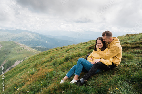 Love in the mountains. A loving couple of Caucasian ethnicity hugging while sitting on the top of the mountain, enjoying each other, the landscape and harmony