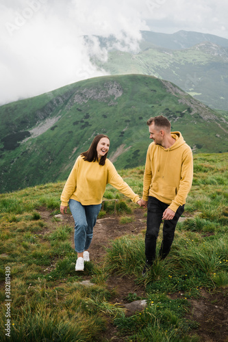 A couple in love is hiking holding hands on the top of mountains and enjoying with a scenic view around them