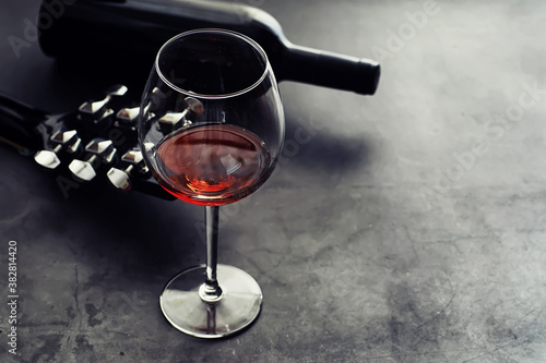Guitar and high glass with red wine on a stone background.