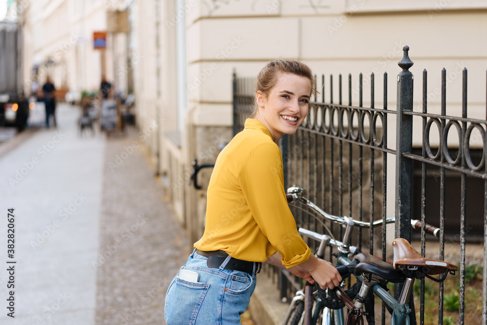 Happy young woman chaining her bike to a fence