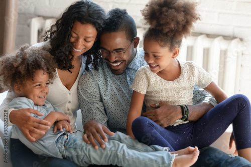 Smiling bonding mixed race family enjoying relaxed playtime on weekend at home. Happy affectionate married couple having fun with adorable biracial small daughter and son together in living room.