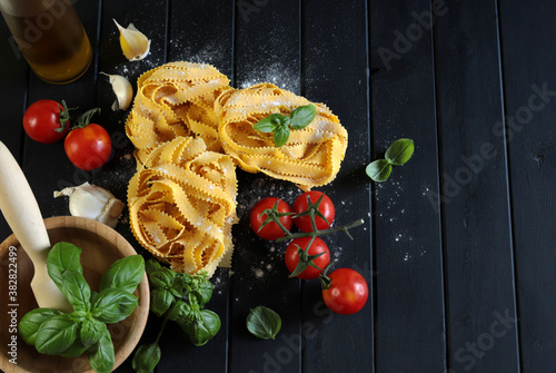 Pasta italiana. Pasta pappardella, pomodori, basilico fresco e aglio su sfondo scuro. Vista dall'alto. photo