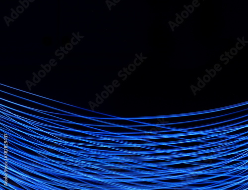 Long exposure photograph of neon blue colour in an abstract swirl, parallel lines pattern against a black background. Light painting photography.