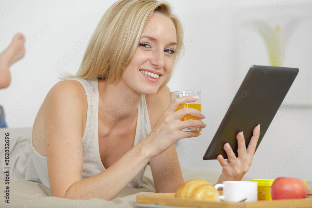 woman holding tablet while having breakfast in bed woman holding tablet while having breakfast in bed