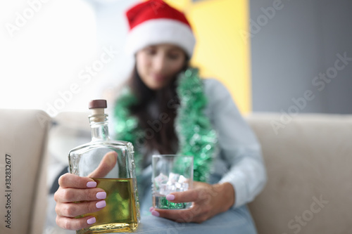 Woman in red santa hat holds a glass of ice and a bottle of whiskey close-up. Celebrating christmas and new year alone concept.