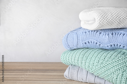 Stack of folded warm sweaters on wooden table. Space for text