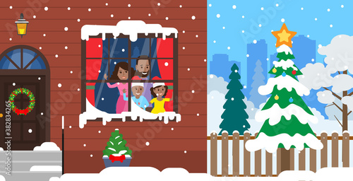 merry christmas and happy new year african american family look through the window on falling snow and decorated spruce