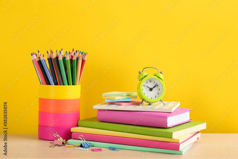 Different school stationery and alarm clock on table against yellow background. Back to school