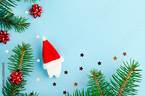 medical dental christmas on blue background with fir branches, creative toy tooth in red santa hat, copy space, place for text