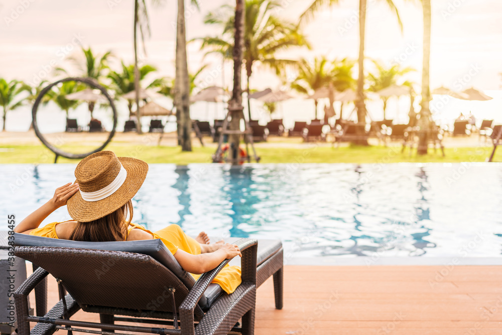 Obraz premium Young woman traveler relaxing and enjoying the sunset by a tropical resort pool while traveling for summer vacation