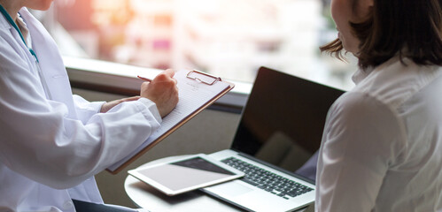 Professional medical doctor in white uniform gown coat interview counseling female patient: Physician writing on patient chart while consultation: Hospital/ clinic healthcare professionalism concept
