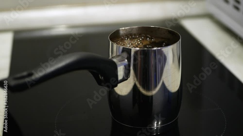 Coffee boils in a steel coffee maker, black glass-ceramic induction cooker, close-up cezve