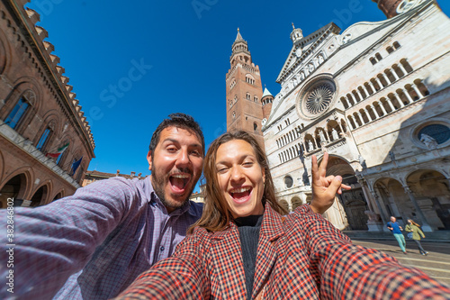 Photos happy tourist couple visiting the city of Cremona taking selfie in the middle of main square of Cremona with Cathedral, baptistery and Torrazzo bell tower