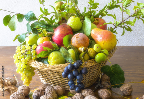 Autumn season and nature concept  beautiful assortment of fruits in a basket on a wooden table. Composition of a variety of organic fruits  Red and white grapes  apples  pomegranate  figs and nuts.