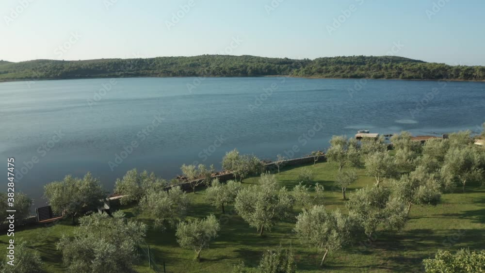 Aerial wide shot of a beautiful landscape in Croatia. Garden and lagoon in the foreground, small hills with trees in the background. Drone flies over the garden. Small boat visible at a peer. Aerial wide shot of a beautiful landscape in Croatia. Garden and lagoon in the foreground, small hills with trees in the background. Drone flies over the garden. Small boat visible at a peer.