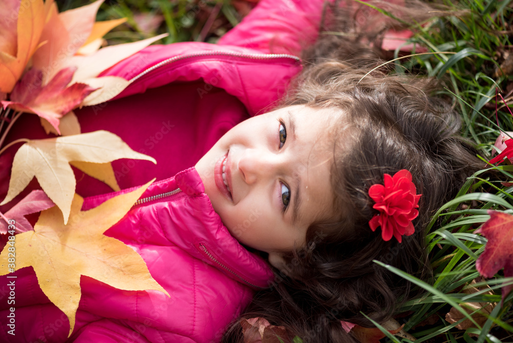 Naklejka premium Girl with autumn leaves. Portrait of a girl on a background of grass and leaves.