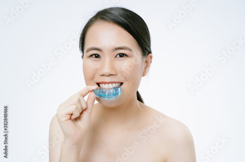 Beautiful young Asian woman smiling with bare shoulders and holding using invisible braces or trainer isolated over white background. Invisalign orthodontics concept