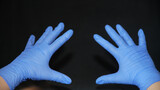 Hand-washing to protect against coronavirus (COVID-19) Two hands covered in blue surgical gloves, pointing forward, fingers apart, on black background