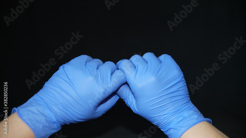 Hand-washing to protect against coronavirus (COVID-19) Two hands covered in blue surgical gloves, holding by thumb and forefinger, on black background
