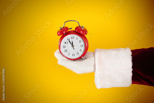 Santa Claus holding alarm clock on yellow background, closeup. Christmas countdown