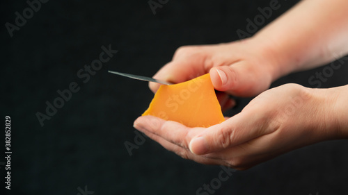 A knife in her hand, she slices in an old piece of cheese, called mimolette, on a black background	