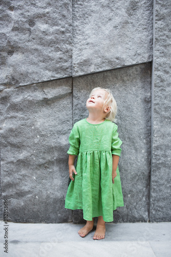 Cute blond little baby girl is looking up wearing green linen dress