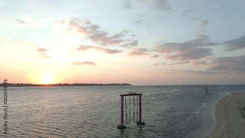 Girl walking on sandy beach with love swing in water during sunset in background.Gili Air,Asia. Girl walking on sandy beach with love swing in water during sunset in background.Gili Air,Asia.