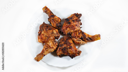 Chicken legs marinated in spices, grilled, arranged in a white plate, on a woody background	
