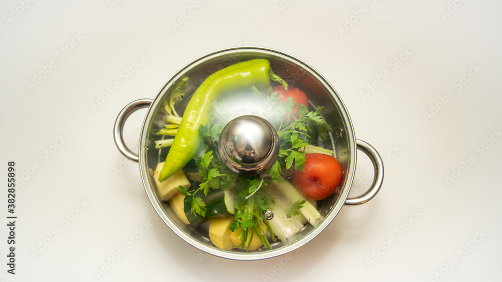 Steel pot, filled with various vegetables and covered with a glass lid, close-up