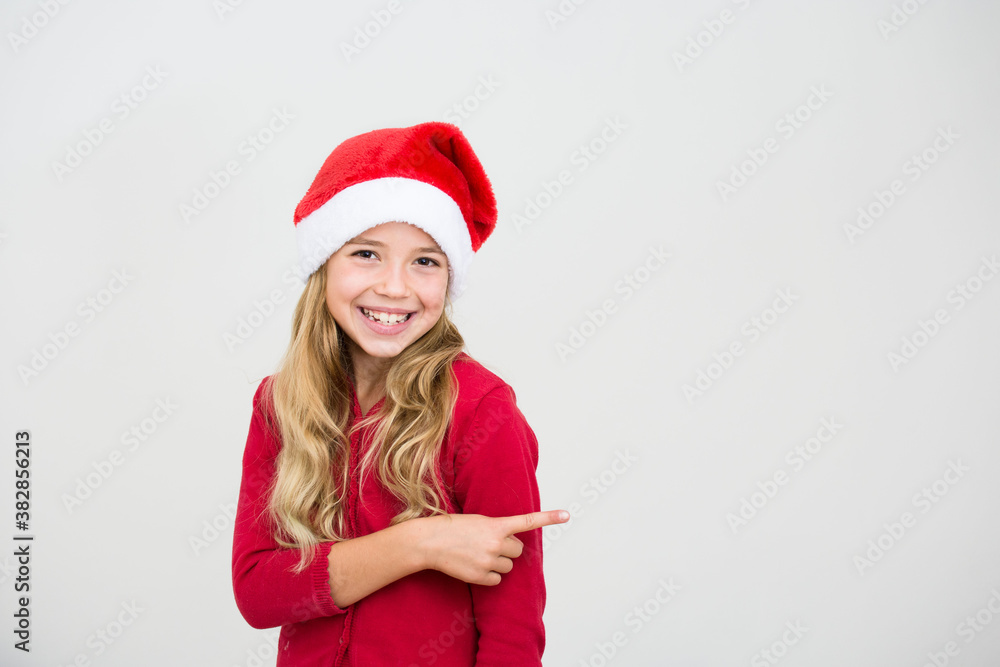 Young smiling, girl in santa hat show with index finger isolated on white background. Kid point. Christmas advertising concept,banner copy space. Young smiling, girl in santa hat show with index finger isolated on white background. Kid point. Christmas advertising concept,banner copy space.