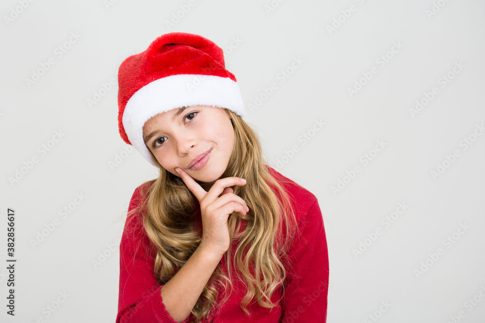 Thoughtful young girl in red dress and santa hat isolated on white background, banner copy space. Christmas congratulation concept. Thoughtful young girl in red dress and santa hat isolated on white background, banner copy space. Christmas congratulation concept.