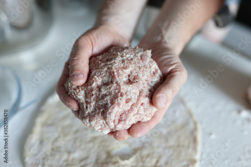 Male hands hold minced meat in palms. Circle of dough in flour on table.