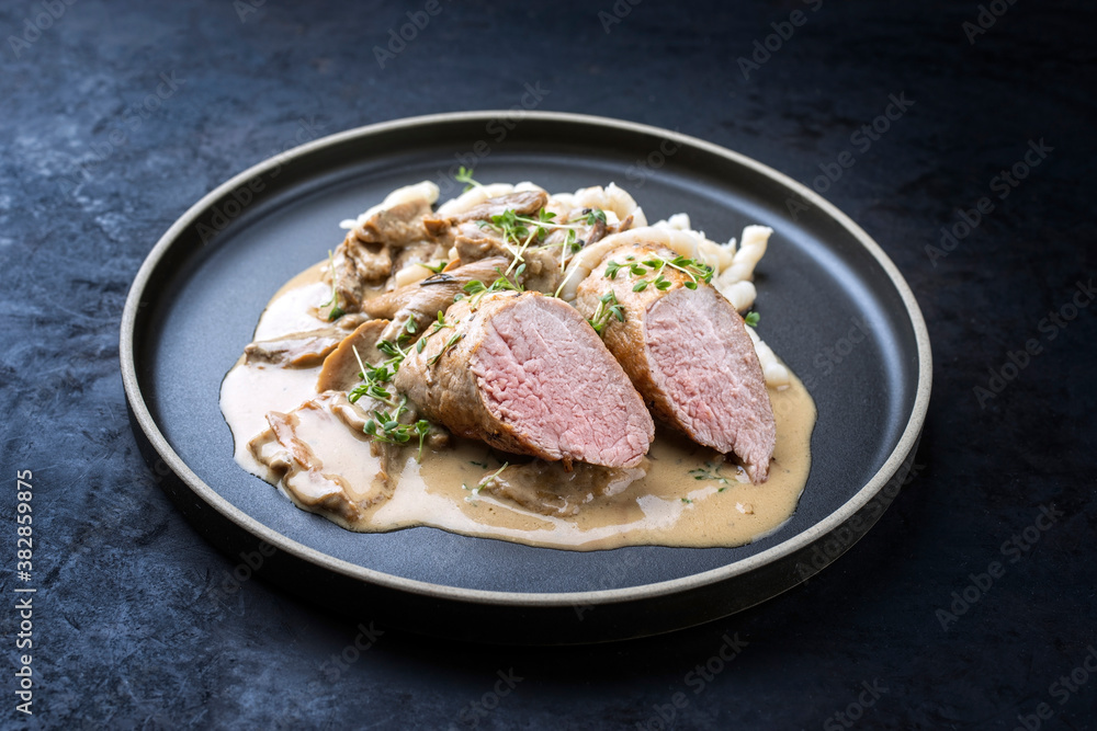Modern style traditional barbecue Iberian pork filet medaillons in cream sauce with mushrooms and herbs offered as close-up on a Nordic design plate with copy space Modern style traditional barbecue Iberian pork filet medaillons in cream sauce with mushrooms and herbs offered as close-up on a Nordic design plate with copy space