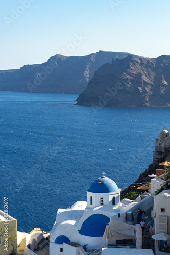 View of Santorini, with typical blue dome church, caldera, sea and flags. Portrait format