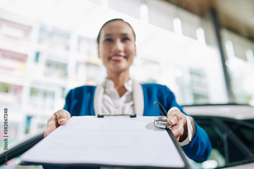Smiling pretty car dealership manager giving vehicle purchase agreement and electronic car keys to customer Smiling pretty car dealership manager giving vehicle purchase agreement and electronic car keys to customer