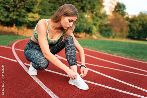 Beautiful female runner tying shoelaces in the running track