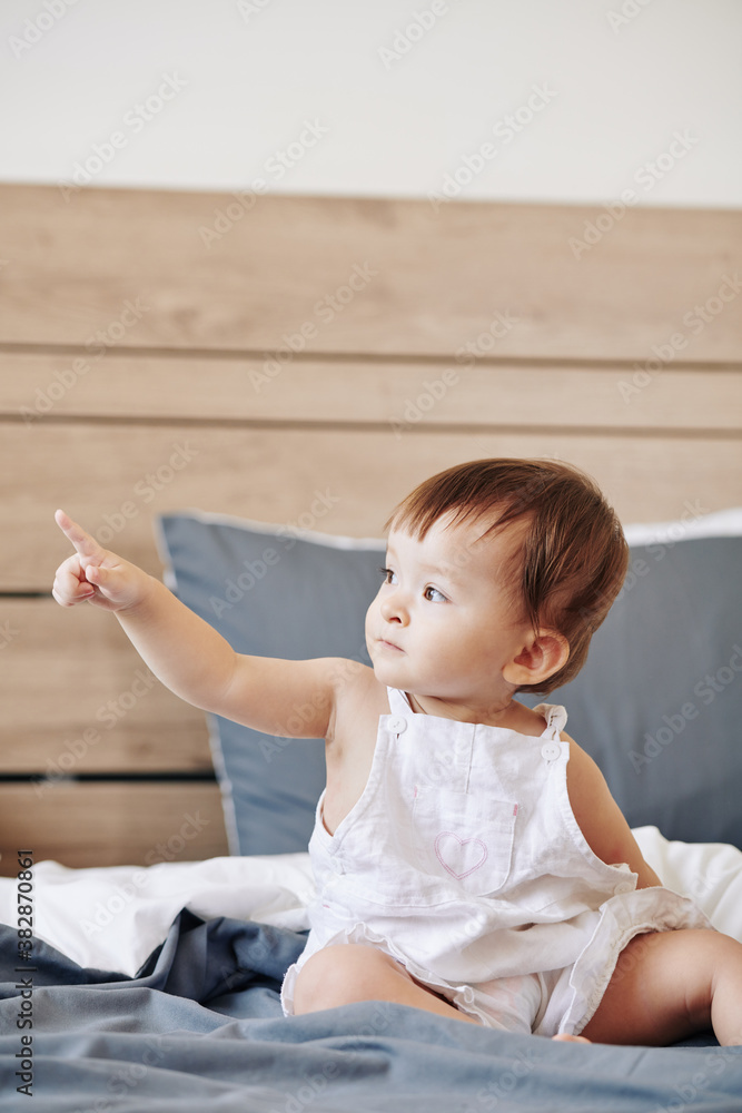 Curious little kid sitting on bed and pointing with finger Curious little kid sitting on bed and pointing with finger